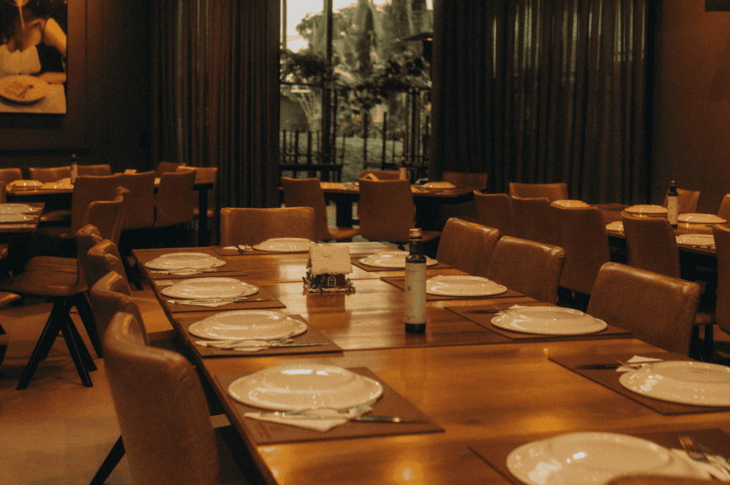 Warmly lit Singapore fine dining interior featuring elegantly set wooden tables with white porcelain, wine bottles, and soft textiles—evoking the refined ambiance, hospitality precision, and sensory immersion that define a signature luxury dining experience.