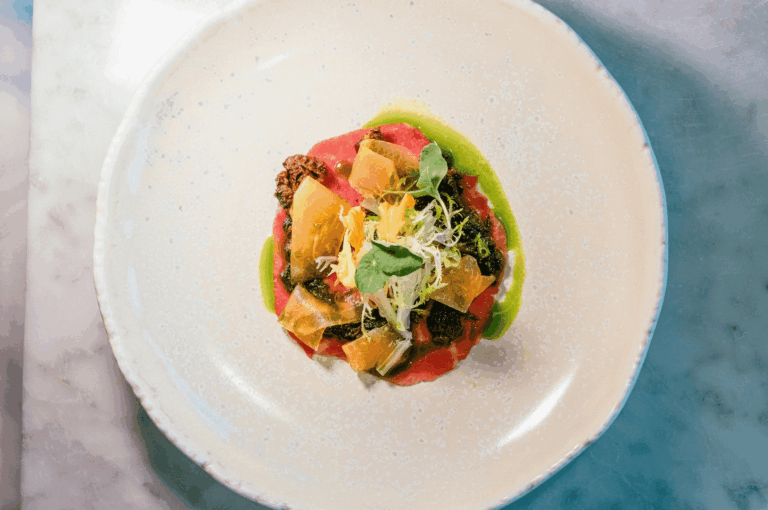 A refined plant-based dish plated on a white rimmed plate over a marble counter, featuring vibrant greens, delicate garnishes, and fine-dining presentation — suitable for a Singapore-focused article on Michelin-level vegan cuisine.