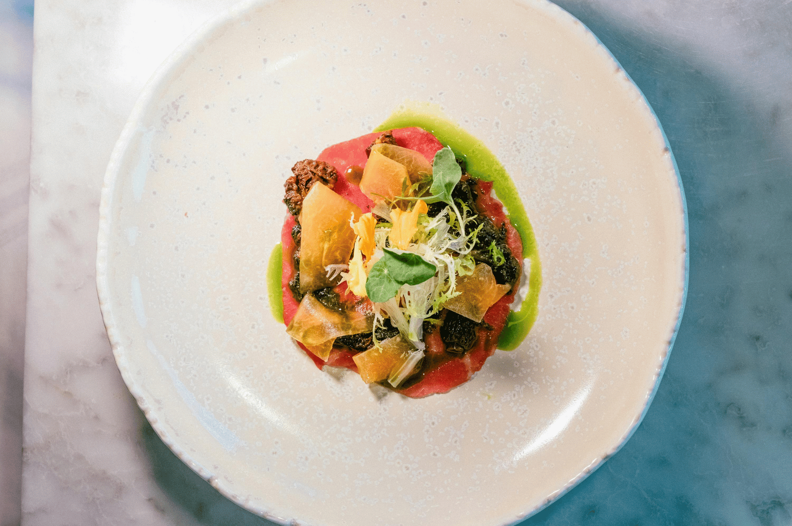 A refined plant-based dish plated on a white rimmed plate over a marble counter, featuring vibrant greens, delicate garnishes, and fine-dining presentation — suitable for a Singapore-focused article on Michelin-level vegan cuisine.