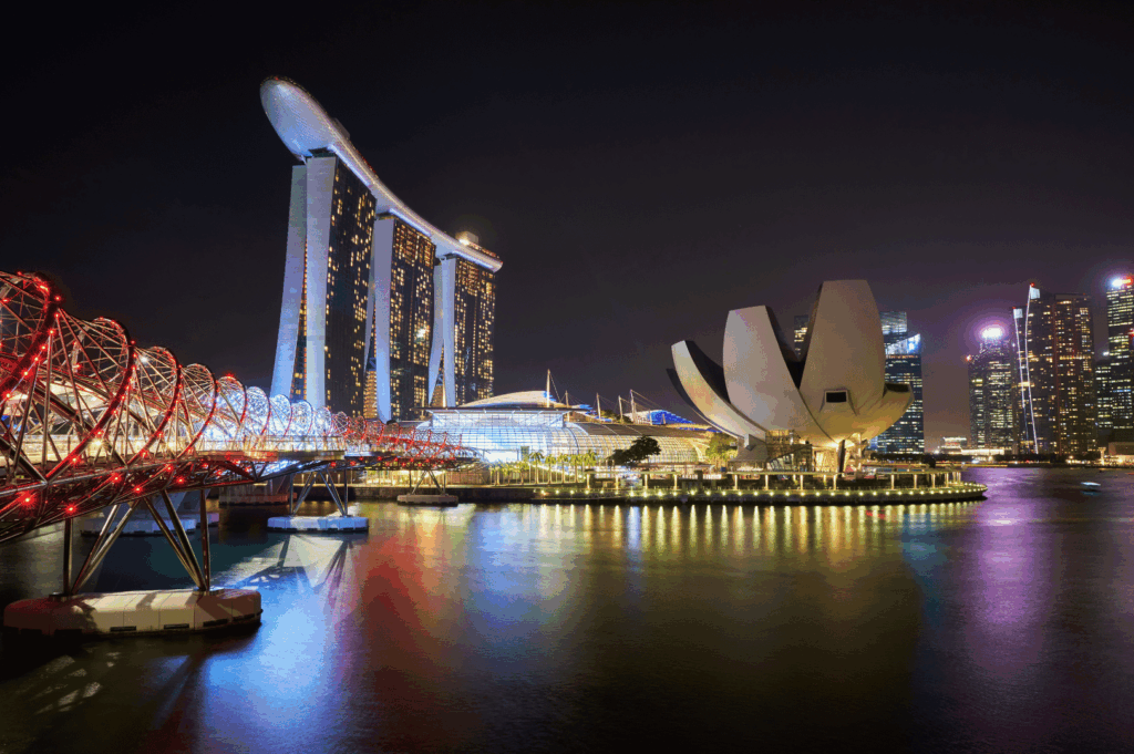 Nighttime view of Marina Bay in Singapore, featuring the illuminated Marina Bay Sands hotel, ArtScience Museum, and Helix Bridge reflected in the bay’s waters—an iconic urban skyline that frames some of the city’s most scenic waterfront restaurants.