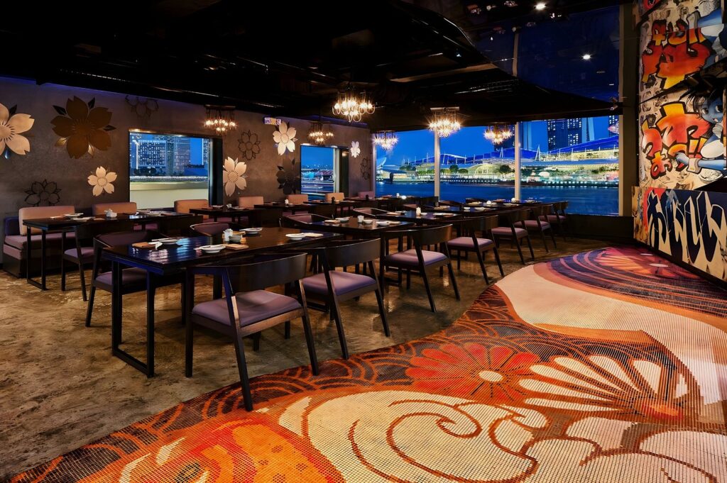 Dining hall at Kinki Restaurant + Bar, Singapore: long black tables, purple chairs, chandeliers, floral wall art, and night city views.