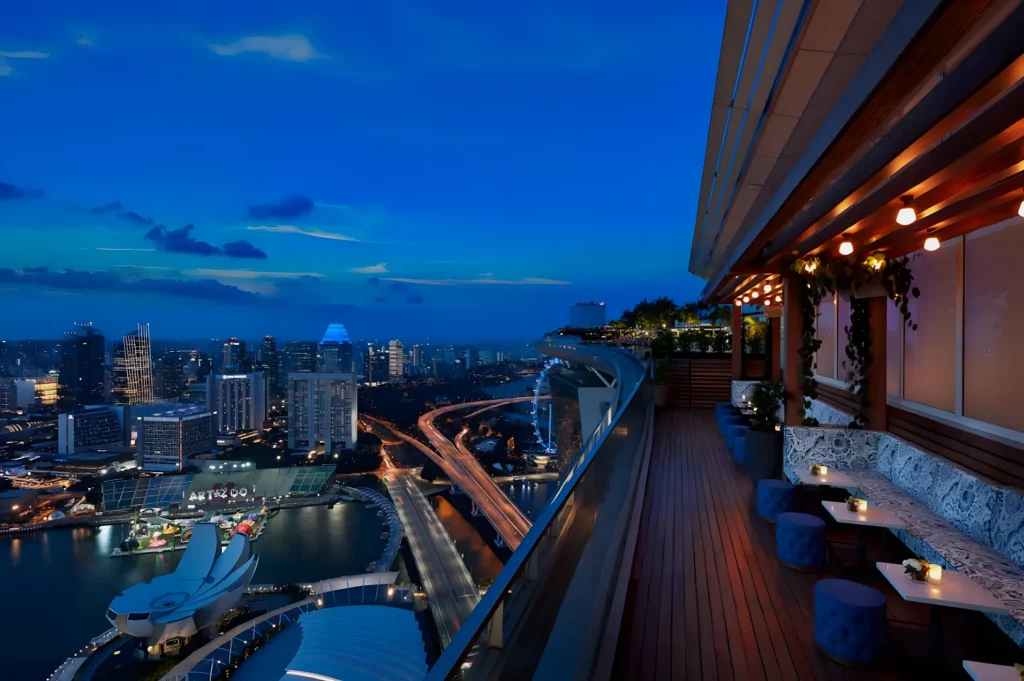 Rooftop lounge at dusk with city skyline view. Ambient lighting, cozy seating, and a panoramic cityscape create a tranquil and luxurious atmosphere.