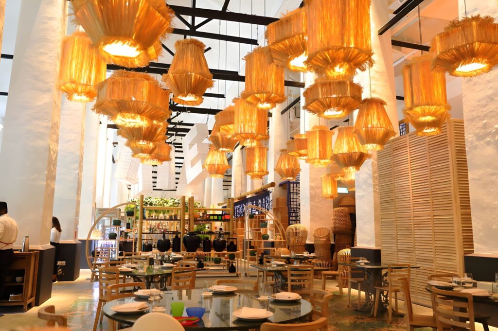 Elegant interior view featuring high ceilings, soft orange lighting, and stacked wicker decor; a refined, modern dining space in Candlenut, Singapore.