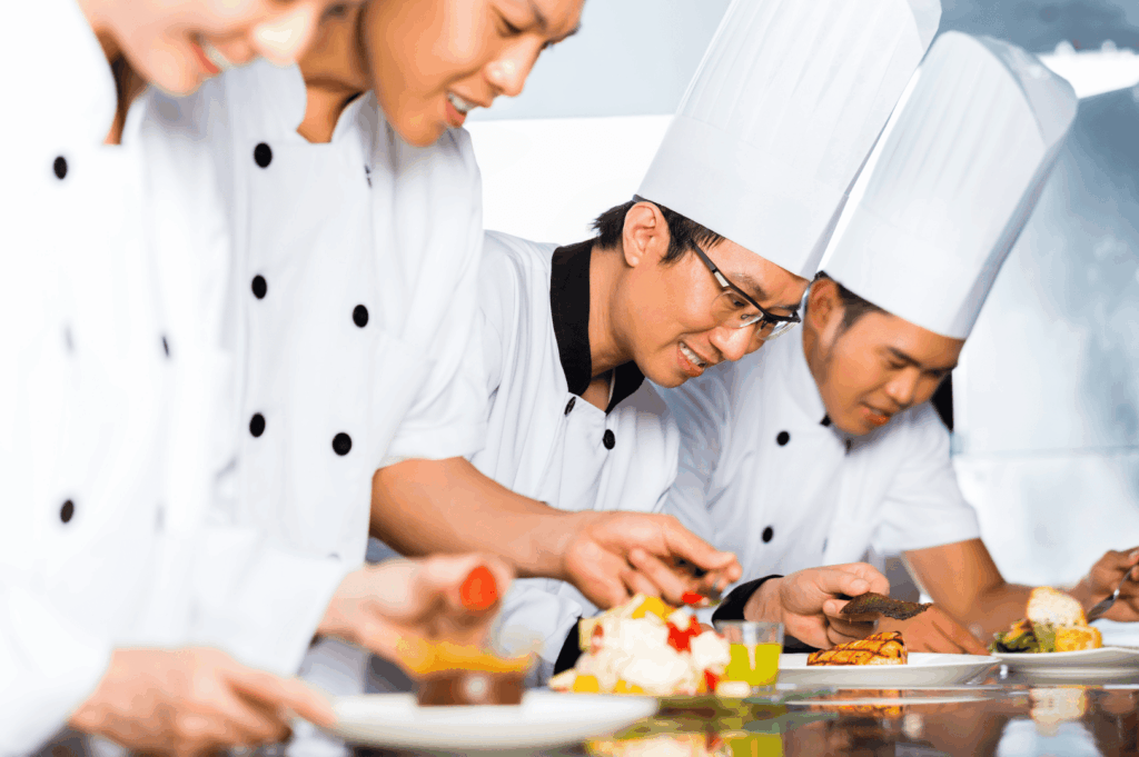 Group of chefs in white uniforms and tall hats plating gourmet dishes in a professional kitchen—capturing the teamwork, culinary excellence, and cooking techniques essential to earning a michelin star. This fine dining environment reflects the standards outlined in the michelin star restaurant guide, where michelin inspectors evaluate restaurants for one michelin star, two michelin stars, or three michelin stars based on five criteria. The chefs’ focus on premium ingredients, seasonal produce, and innovative dishes mirrors the tasting menu experiences offered by fine dining establishments like Summer Pavilion, Saint Pierre, and those at Marina Bay or Ion Orchard. World renowned chefs such as chef louis han, chef yew eng tong, head chef takuya yamashita, chef owner emmanuel stroobant, chef denis lucchi, and chef christophe lerouy lead culinary journeys that blend global influences, japanese cuisine, and exceptional cuisine. Michelin introduced the michelin green star and bib gourmand to recognize sustainability and good restaurant practices in the hospitality industry. Whether guided by a head chef, sous chef, or young chef, this culinary haven showcases the chef’s personality and the pursuit of gastronomic excellence in star restaurants featured in the michelin guide.