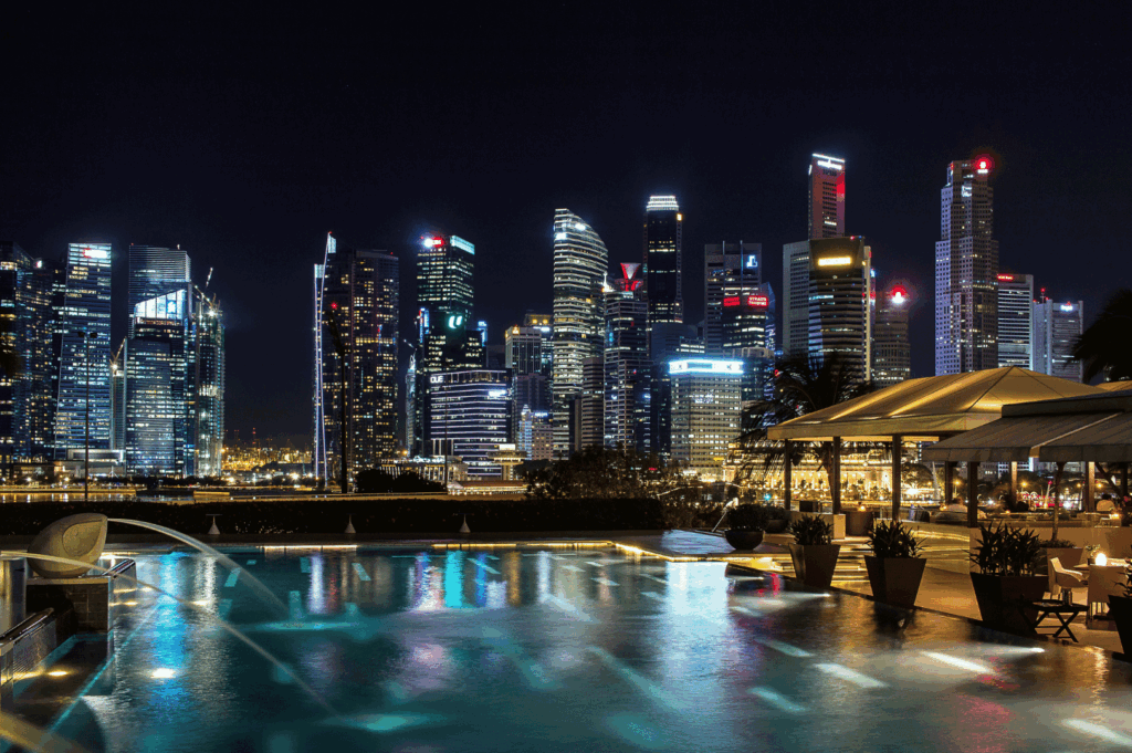 Nighttime view from a rooftop infinity pool overlooking Singapore’s illuminated skyline, with ambient lighting, lounge chairs, and shaded seating evoking luxury and serenity—an elevated urban escape that mirrors the city’s high-end dining experiences.