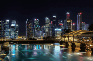Nighttime view from a rooftop infinity pool overlooking Singapore’s illuminated skyline, with ambient lighting, lounge chairs, and shaded seating evoking luxury and serenity—an elevated urban escape that mirrors the city’s high-end dining experiences.