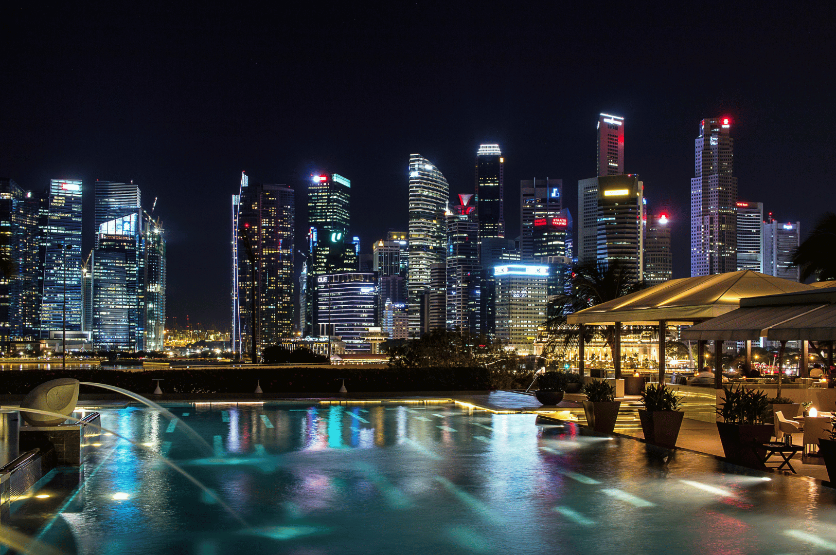 Nighttime view from a rooftop infinity pool overlooking Singapore’s illuminated skyline, with ambient lighting, lounge chairs, and shaded seating evoking luxury and serenity—an elevated urban escape that mirrors the city’s high-end dining experiences.