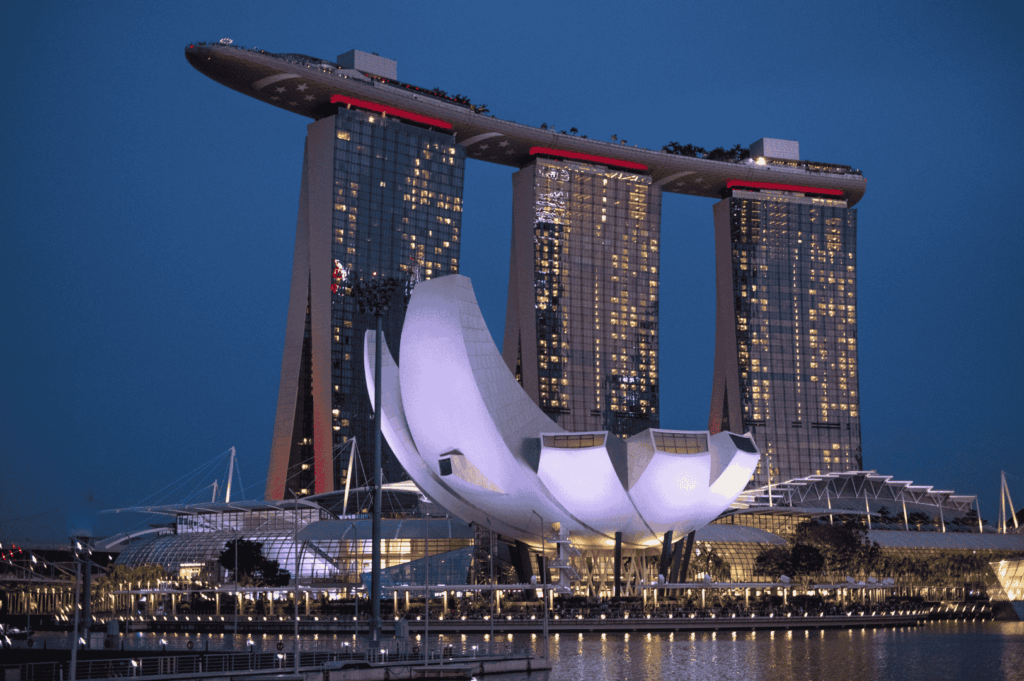 Evening view of Singapore’s iconic Marina Bay Sands towers and lotus-shaped ArtScience Museum, dramatically lit and reflected on tranquil waters—an architectural marvel that anchors the city’s skyline and sets the stage for luxury dining with panoramic vistas.