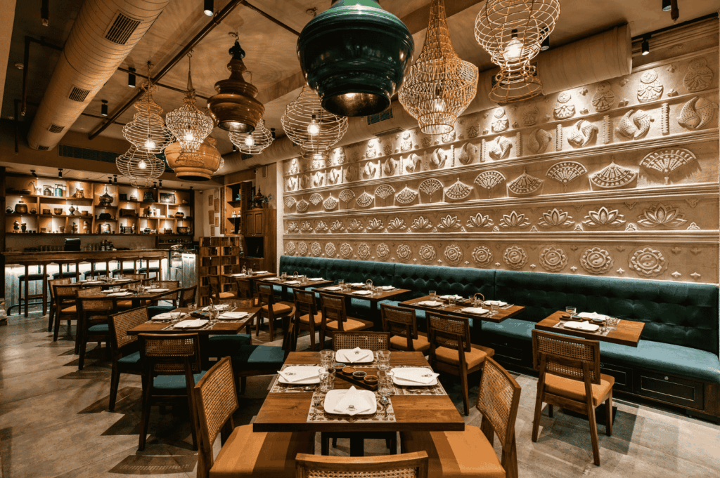 Warmly lit interior of a refined Singapore restaurant blending modern elegance with traditional motifs. Embossed floral and geometric wall patterns frame a row of neatly set wooden tables, each adorned with white napkins and minimalist tableware. Ornate lanterns and wireframe chandeliers hang above, casting a golden glow that evokes the intimate, sensory depth of a curated tasting menu experience.