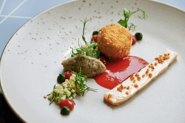 Artfully plated gourmet dish showcasing the precision of Michelin-level dining: a golden croquette, tomato purée swoosh, terrine slice with crispy garnish, eggplant purée, herb dollops, and microgreens arranged on a minimalist white plate. Highlights the contrast between culinary artistry and fine dining presentation.