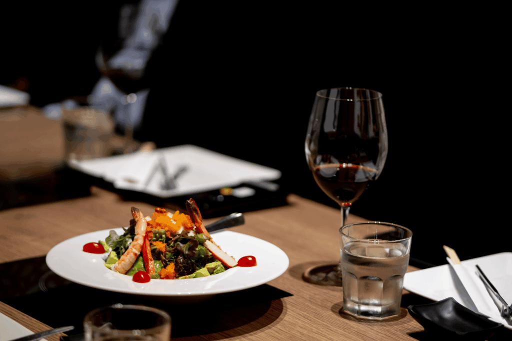 Elegant fine dining table set with shrimp and roe-topped entrée, red wine, and Asian-inspired elements like chopsticks and black napkins. The moody lighting and refined plating evoke the intimacy and sophistication of high-end restaurant experiences—highlighting the nuanced difference from Michelin-style presentation.