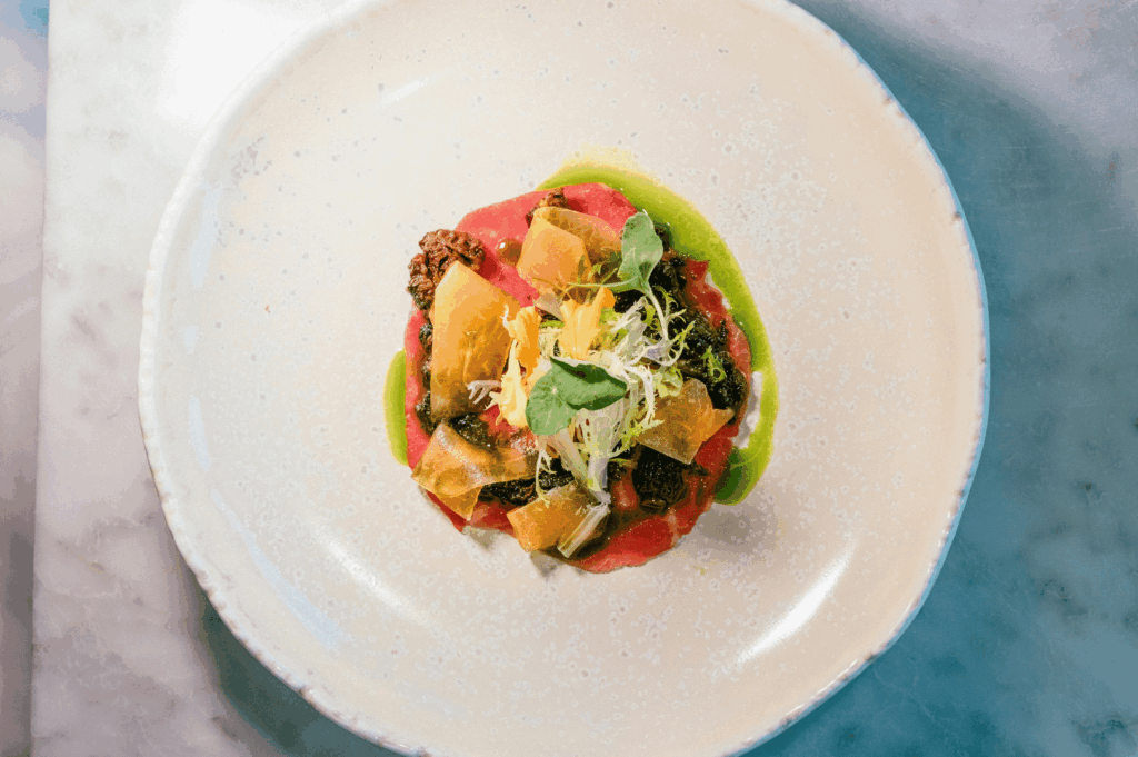 A refined plant-based dish plated on a white rimmed plate over a marble counter, featuring vibrant greens, delicate garnishes, and fine-dining presentation — suitable for a Singapore-focused article on Michelin-level vegan cuisine.