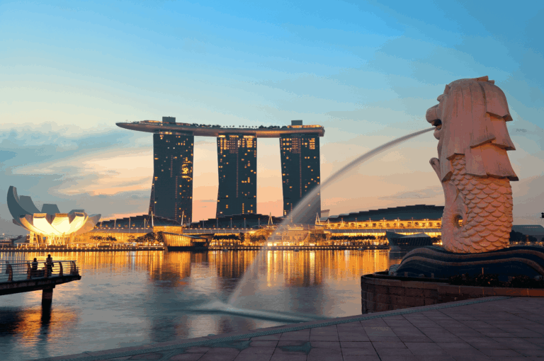 Twilight view of Marina Bay, Singapore, featuring the iconic Merlion spouting water in the foreground, with Marina Bay Sands and the lotus-shaped ArtScience Museum illuminated across the bay. Reflections ripple across the water, evoking the city's blend of architectural grandeur and waterfront serenity—an atmospheric prelude to Singapore’s most scenic dining destinations from the CBD to Sentosa.