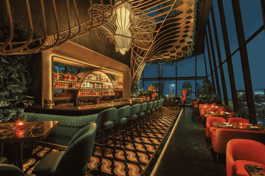 Elegant bar and lounge with teal stools and sculptural ceiling lighting, framed by floor-to-ceiling windows revealing Singapore’s night skyline. Candlelit tables and warm ambient glow evoke intimacy and sophistication—an elevated stop on the city’s scenic dining map from the CBD to Sentosa.