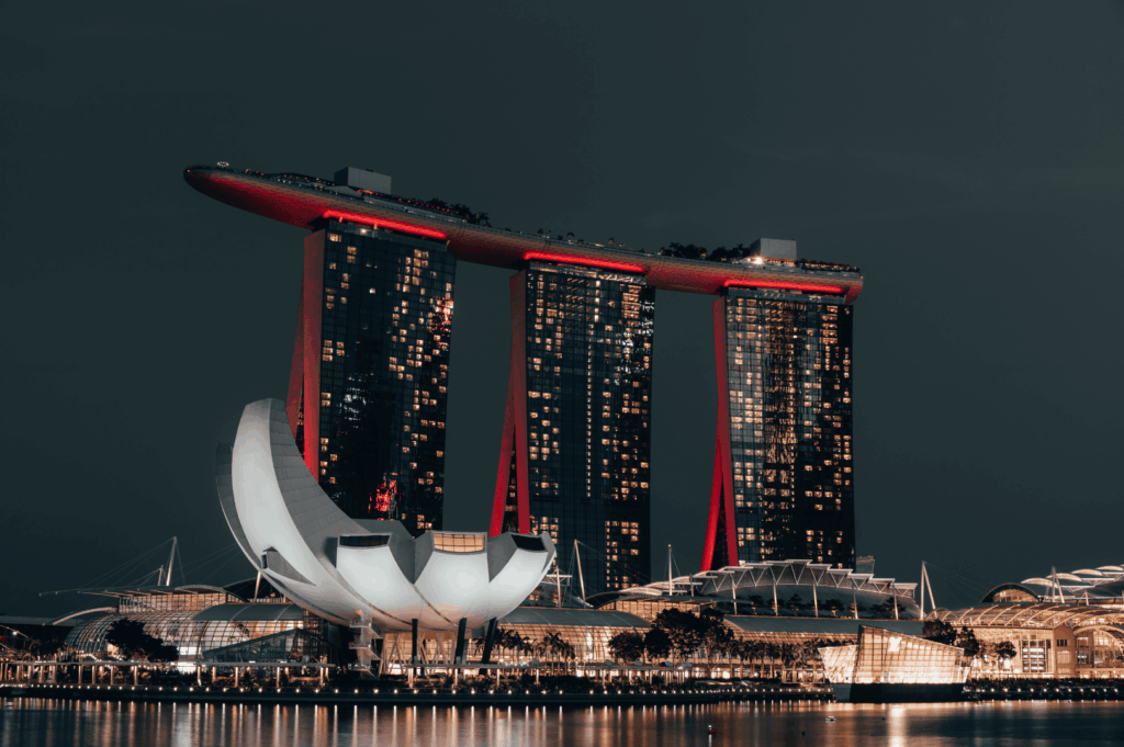 Night view of Marina Bay Sands with its three towers aglow in red, crowned by the boat-shaped sky park, alongside the illuminated lotus-like ArtScience Museum. Reflections shimmer across the bay—an iconic moment in Singapore’s scenic dining journey from the CBD to Sentosa.