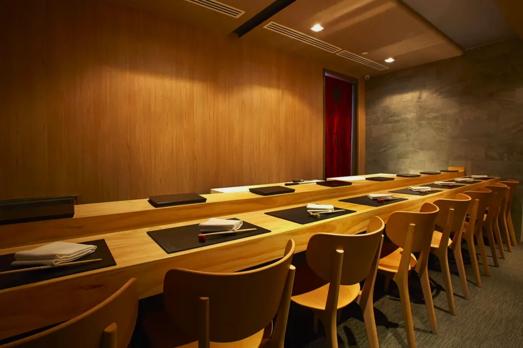 Sleek, modern dining room with a long wooden table set with placemats and napkins. Wooden chairs line the table, creating an elegant, minimalist ambiance.