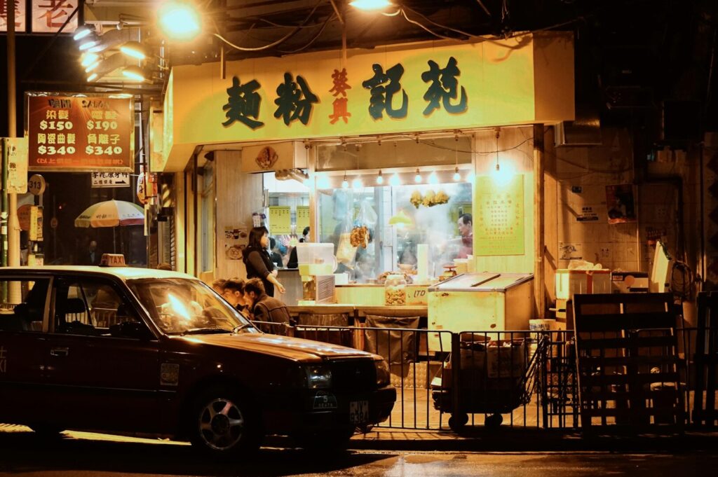 A red car is parked in front of a restaurant known for its Hong Kong street food and Michelin-starred cuisine.