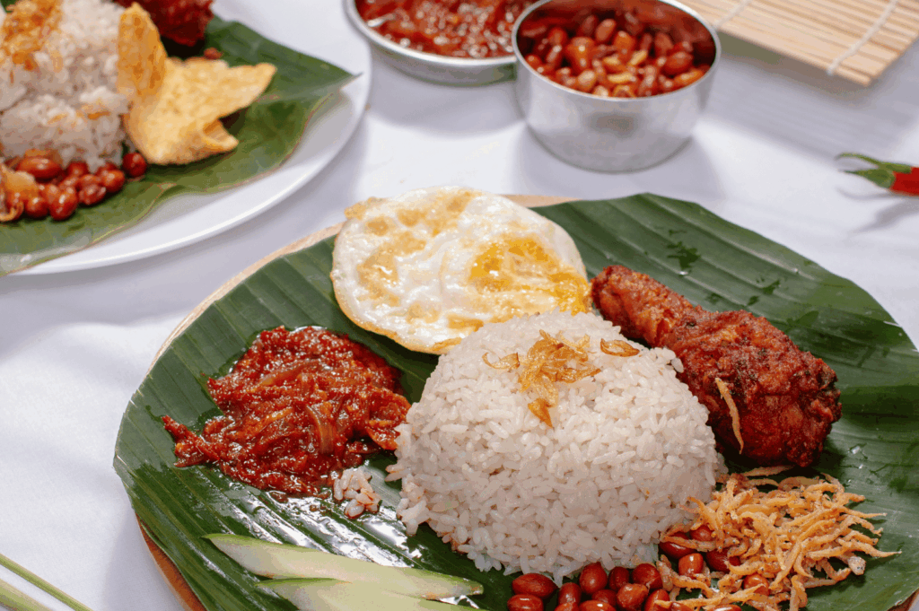 Traditional Nasi Lemak served on banana leaf with fried chicken, egg, sambal, anchovies, peanuts, and cucumber—highlighting the rich flavors and cultural depth of Malaysia’s influence on Singapore’s Michelin street food scene. Would you like a version that leans more into editorial voice or first-timer accessibility?