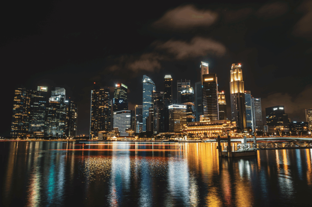 Singapore skyline at night with illuminated skyscrapers reflecting on Marina Bay, showcasing the city’s vibrant urban evolution and waterfront dining allure.