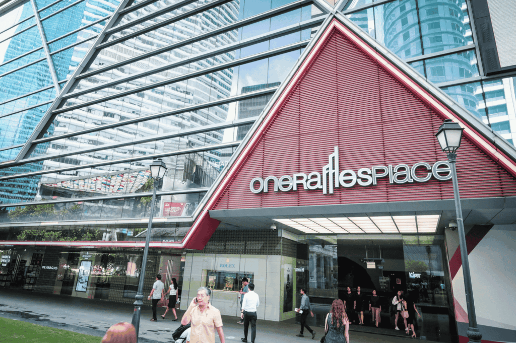 Exterior view of One Raffles Place in Singapore’s central business district, featuring its iconic red triangular facade and glass architecture—an emblem of the city’s evolving skyline and upscale dining scene.