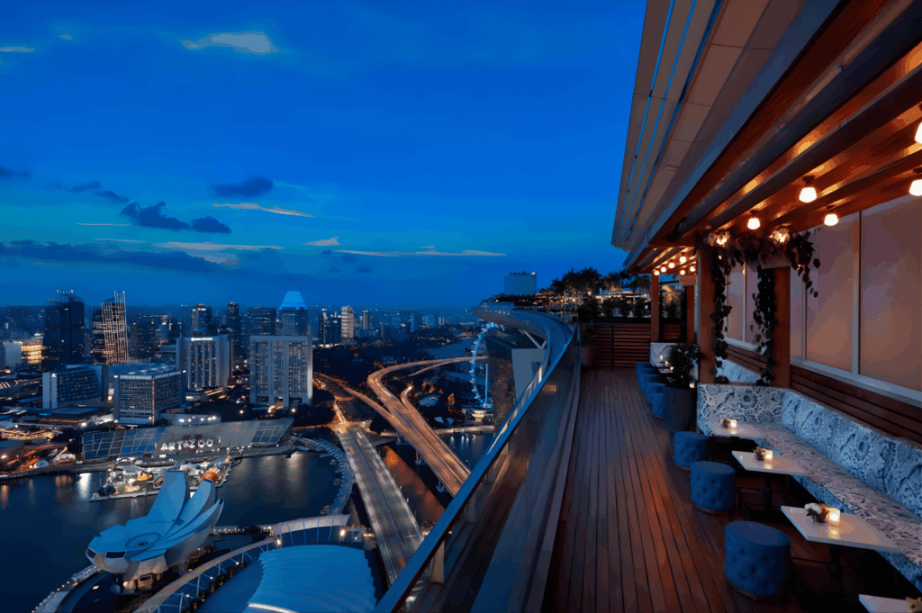 Rooftop lounge in Singapore at dusk with cozy seating, ambient lighting, and panoramic views of the city skyline—capturing the fusion of elevated dining and urban sophistication.