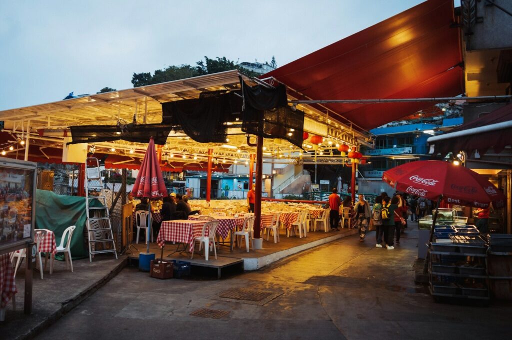 A vibrant hawker food stall in Singapore with tables and chairs arranged under a protective umbrella for diners.