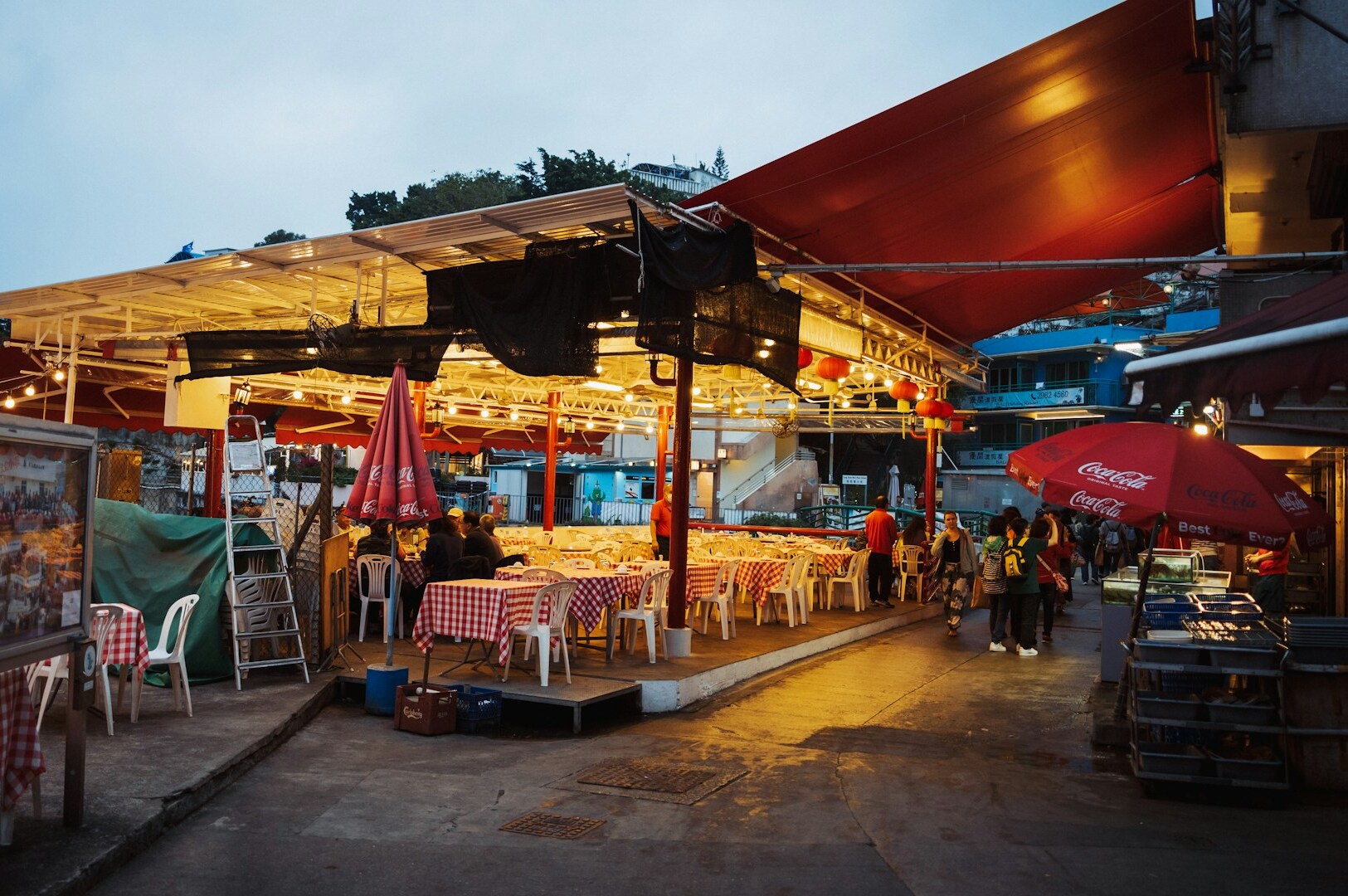 A vibrant hawker food stall in Singapore with tables and chairs arranged under a protective umbrella for diners.