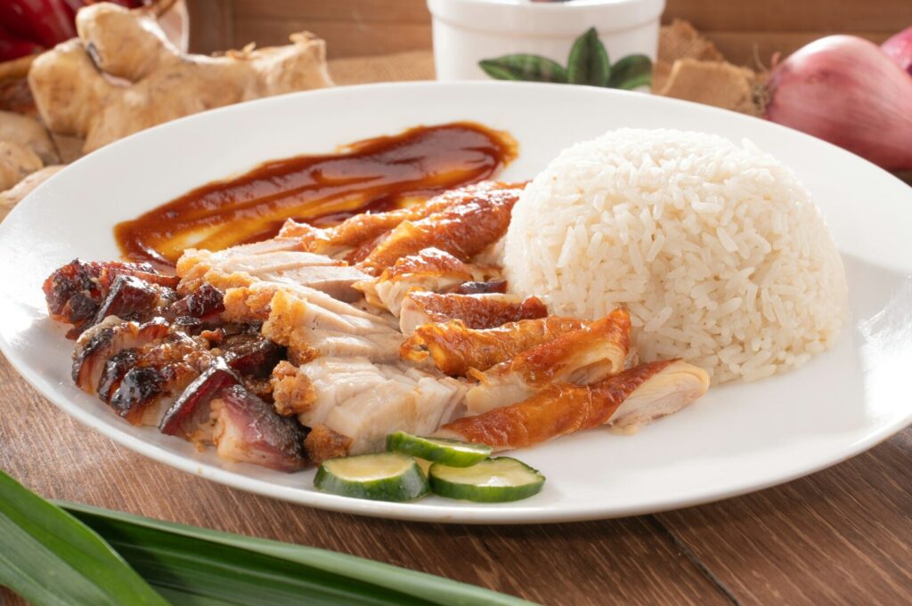 A serving of chicken rice, showcasing succulent chicken pieces atop a mound of steamed rice, accompanied by garnishes.