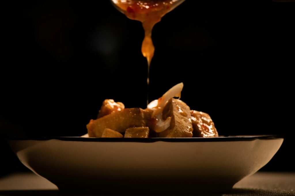 A spoon pouring sauce over a bowl of Peranakan food at a mid-range Singaporean restaurant.