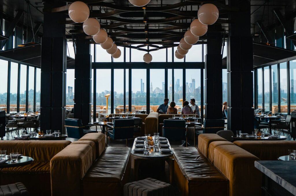 The image depicts an elegant fine dining restaurant featuring a sophisticated dining room with panoramic city views through floor-to-ceiling windows. This modern space, perfect for special occasions, showcases quality ingredients and traditional flavors, creating a refined atmosphere for diners to enjoy their meal while overlooking the stunning skyline of Singapore.