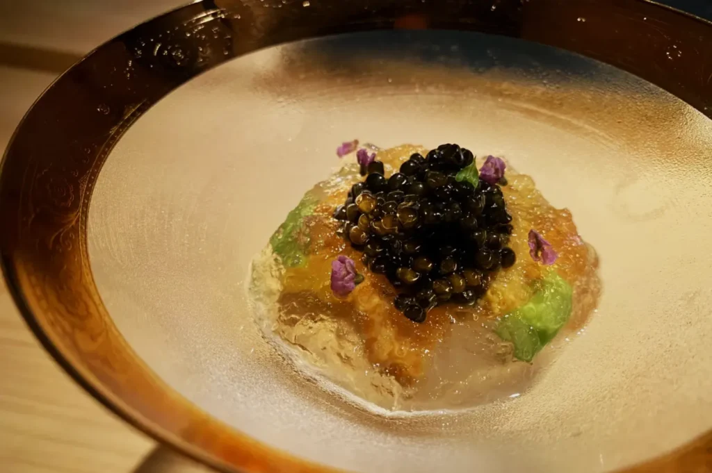 A delicate dish with caviar, served on translucent gelatin, garnished with purple flowers and herbs, in a textured glass bowl, evokes elegance.