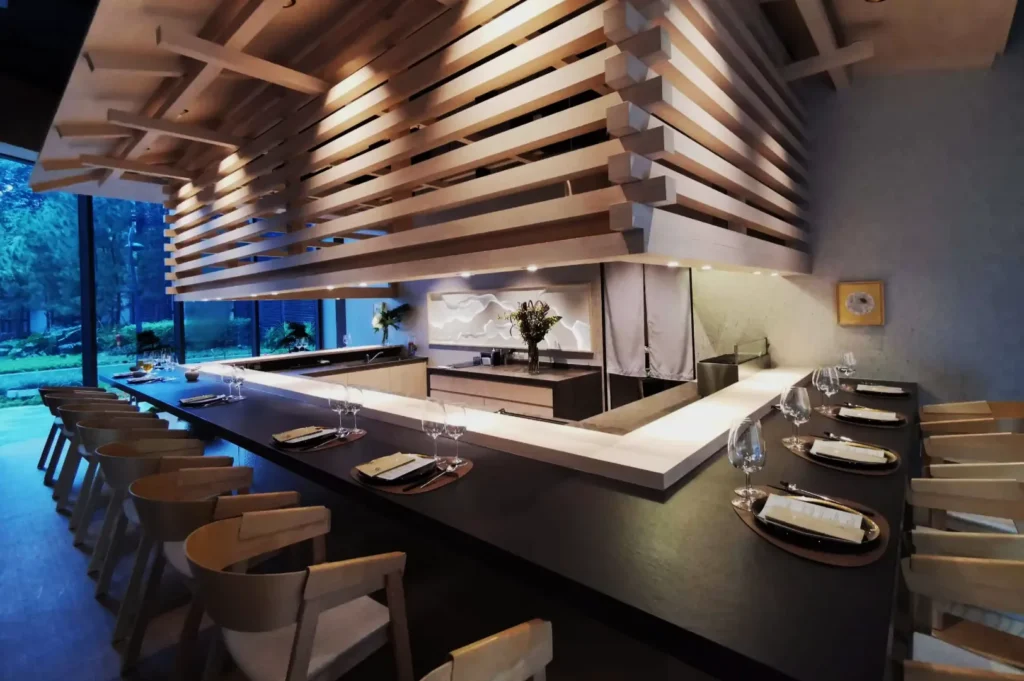 Modern restaurant interior featuring a sleek, minimalist design with wooden elements. Set dining area with elegant table settings and soft lighting.