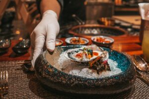 A hand presenting a bowl of oysters on ice, highlighting a gourmet offering from a Michelin Omakase in Singapore.