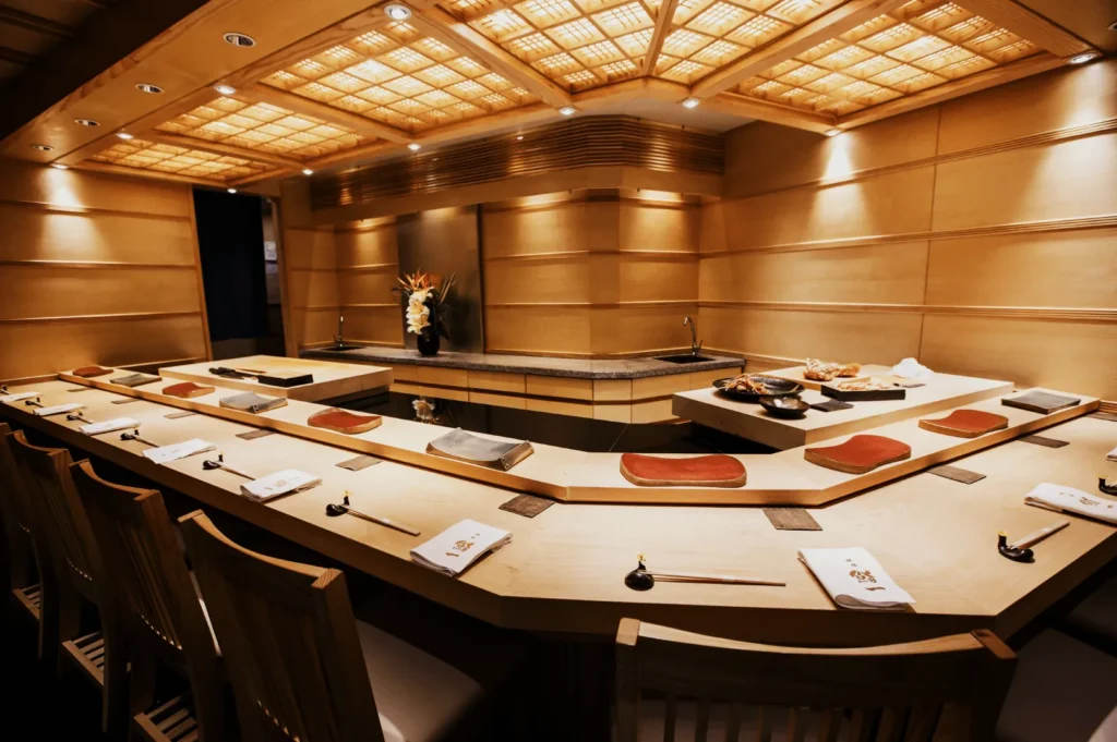 Elegant sushi restaurant with a U-shaped wooden bar, set for dining with neatly placed chopsticks and napkins. Warm lighting creates an inviting ambiance.