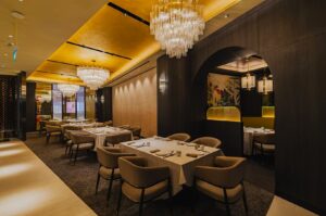 Elegant restaurant interior with warm lighting and crystal chandeliers. Plush armchairs surround tables with white linens, evoking a luxurious ambiance.