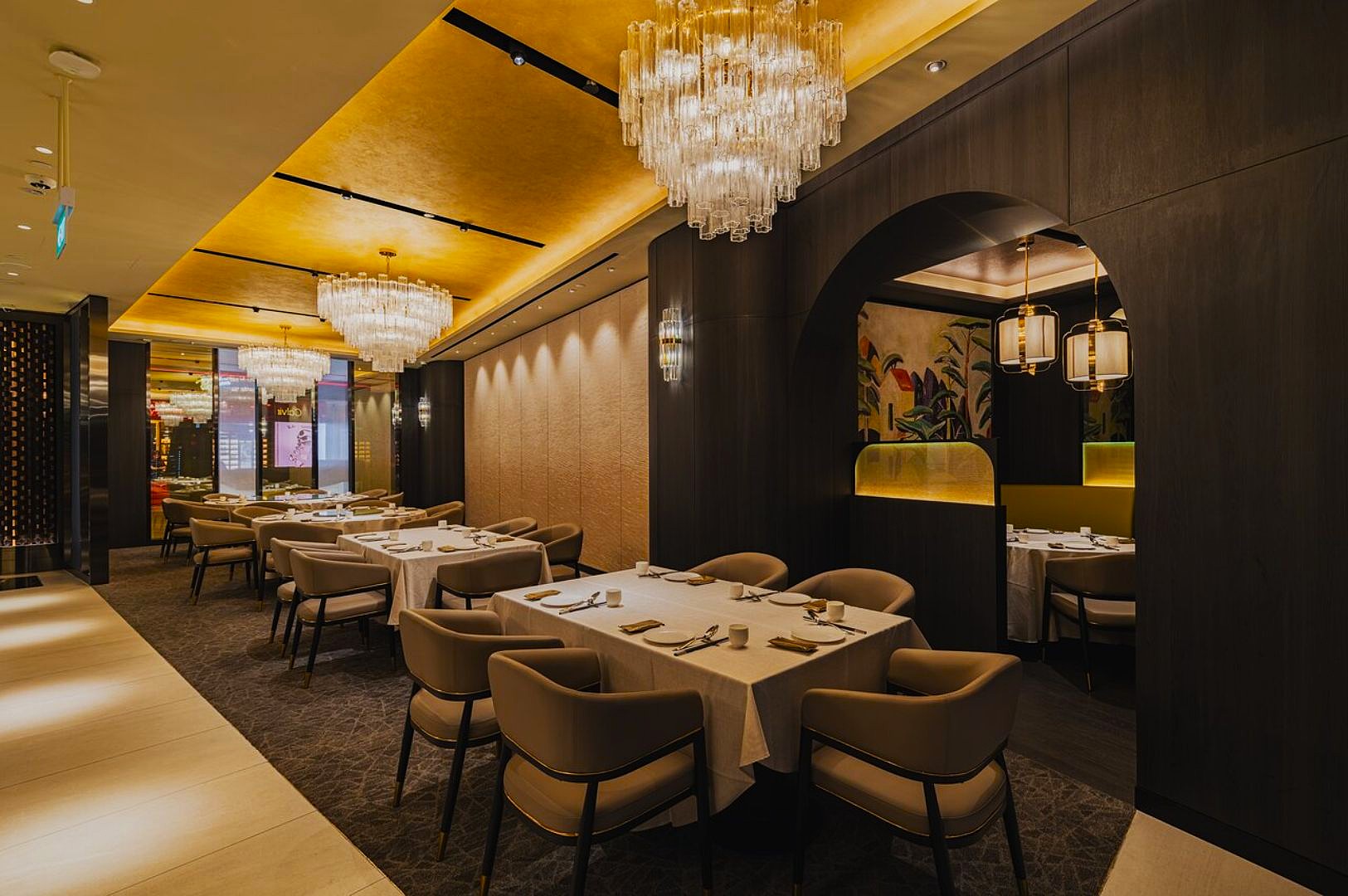 Elegant restaurant interior with warm lighting and crystal chandeliers. Plush armchairs surround tables with white linens, evoking a luxurious ambiance.