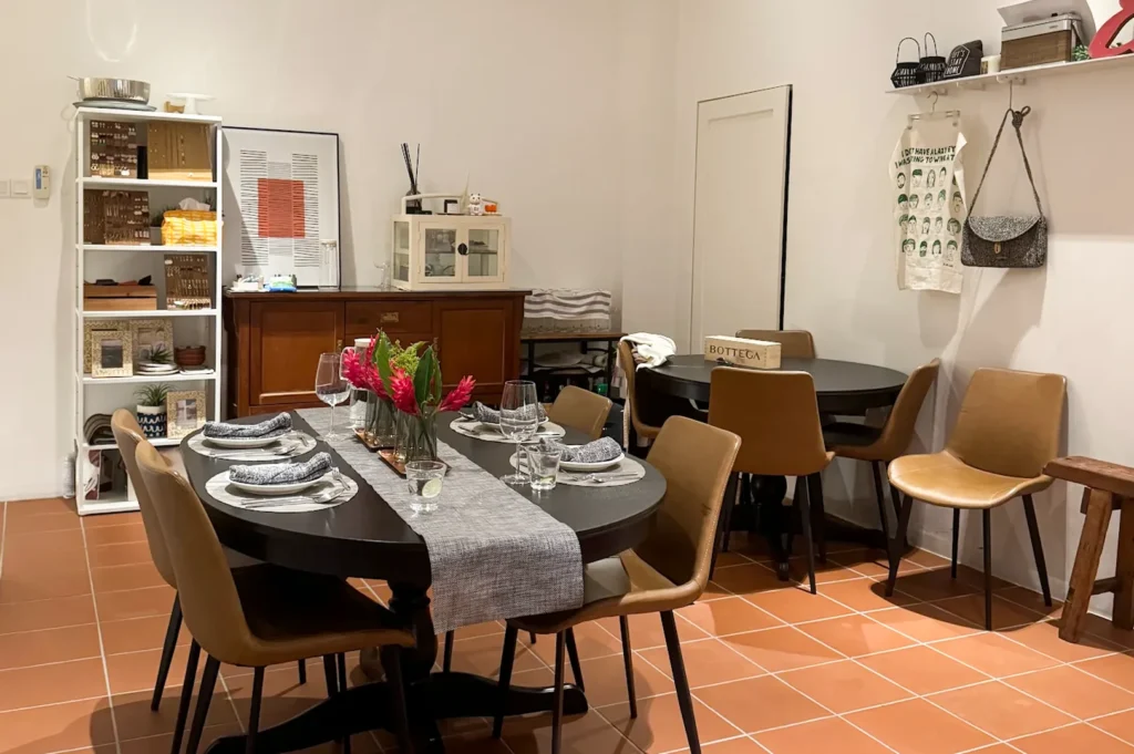 A cozy contemporary dining space with terracotta tile flooring, black oval tables, tan leather chairs, and personalized decor items on shelving.