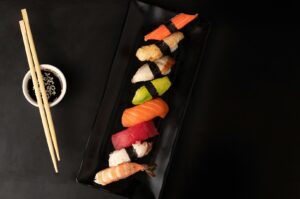 A black plate features various sushi pieces, with chopsticks placed next to the plate, ready for dining.