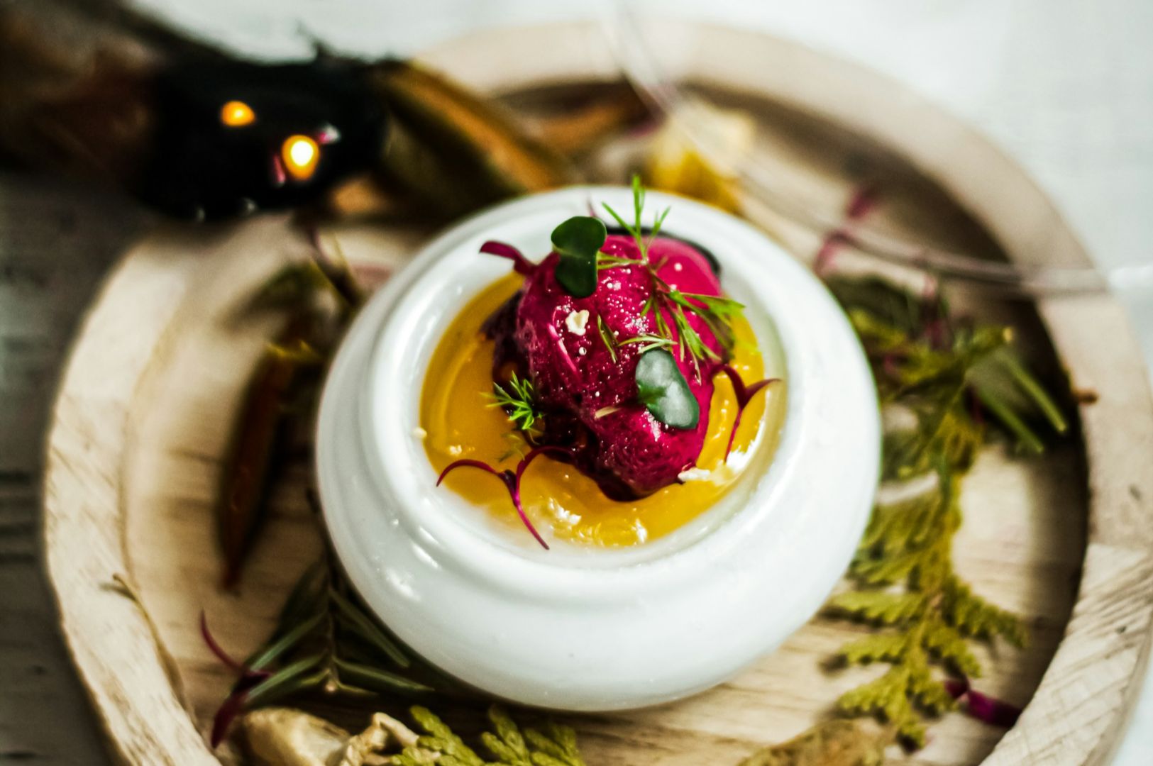 A vibrant dish of deep red sorbet atop bright yellow sauce in a white bowl, garnished with greens, placed on a rustic wooden plate. Elegant and artistic presentation.