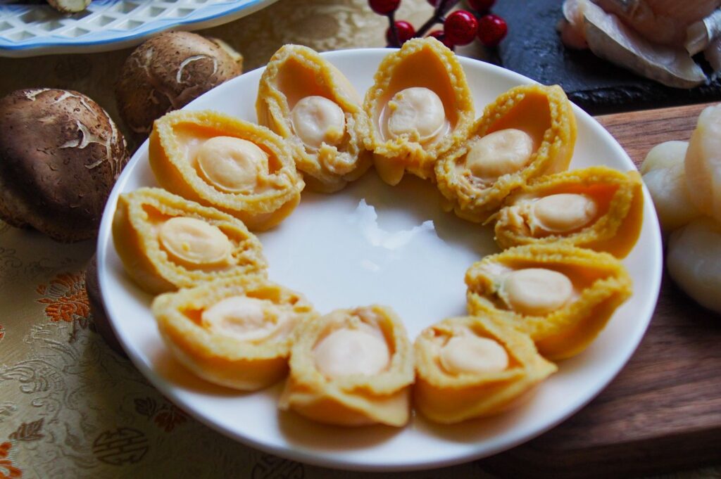 A white plate with sliced abalones, elegantly arranged in a circle. Nearby are fresh mushrooms and red berries, suggesting a gourmet meal.
