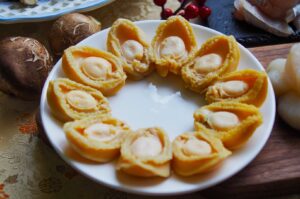A white plate with sliced abalones, elegantly arranged in a circle. Nearby are fresh mushrooms and red berries, suggesting a gourmet meal.