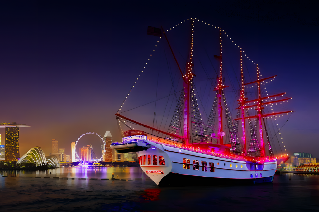 Illuminated tall ship with red sails and string lights docked in a city harbor at night. City skyline glows with neon lights, creating a festive atmosphere.
