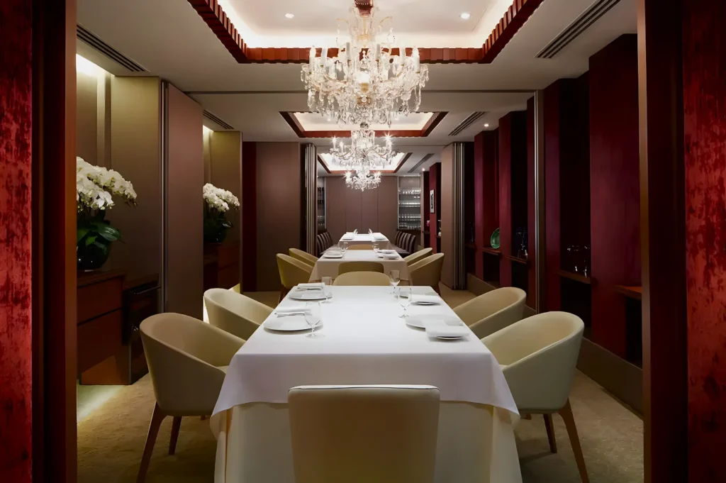 Luxurious dining room with red accents, elegant chandeliers, and long white tables set with plates and glasses. A sophisticated, inviting atmosphere.