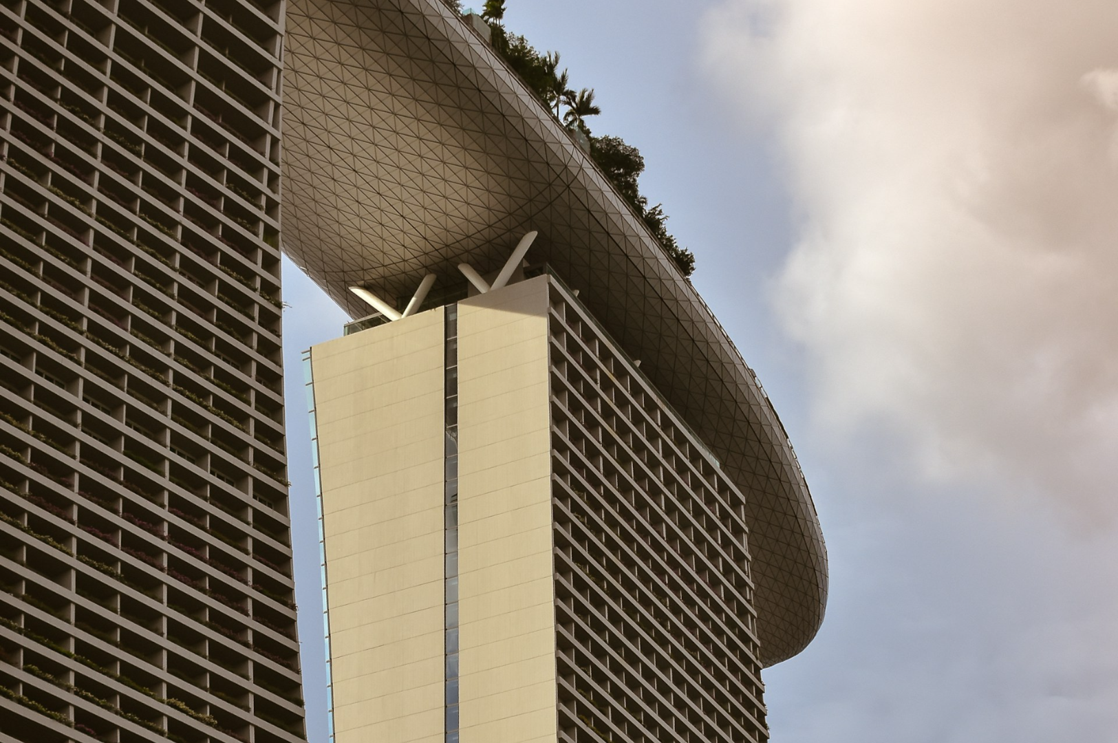 Close-up of Marina Bay Sands' futuristic architecture in Singapore, featuring its iconic, boat-shaped rooftop, set against a cloudy sky.