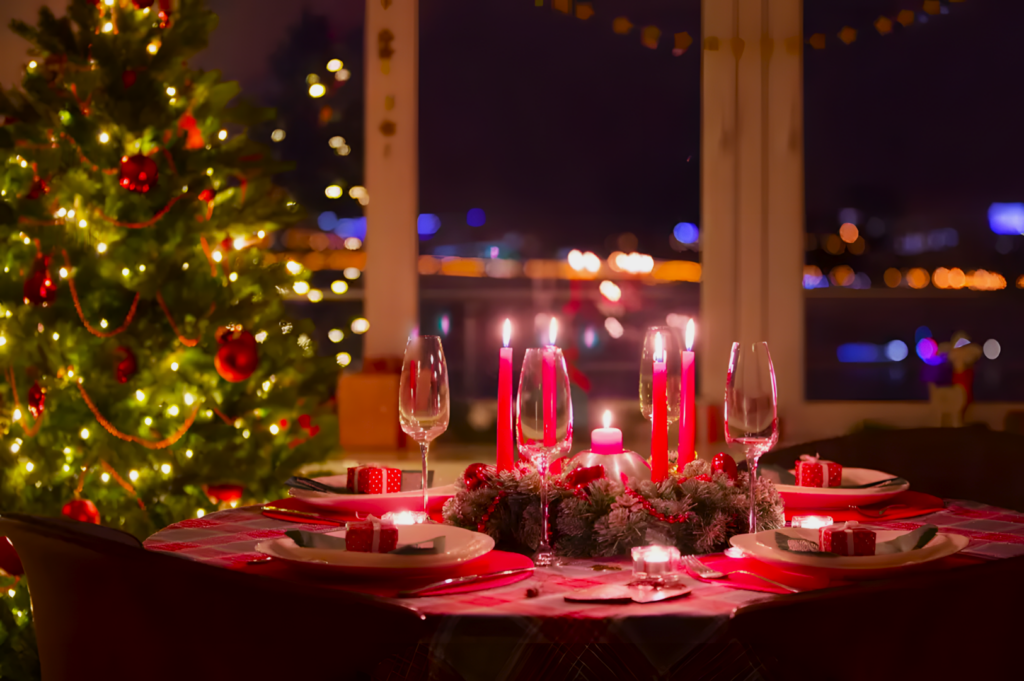 Festive dining scene with a Christmas tree and lights, a table set for dinner with red candles, wine glasses, and wrapped gifts, creating a warm, cozy atmosphere.