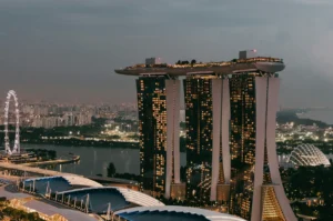 Aerial view of Marina Bay Sands in Singapore at dusk, with illuminated windows and rooftop gardens. The Singapore Flyer is visible on the left.
