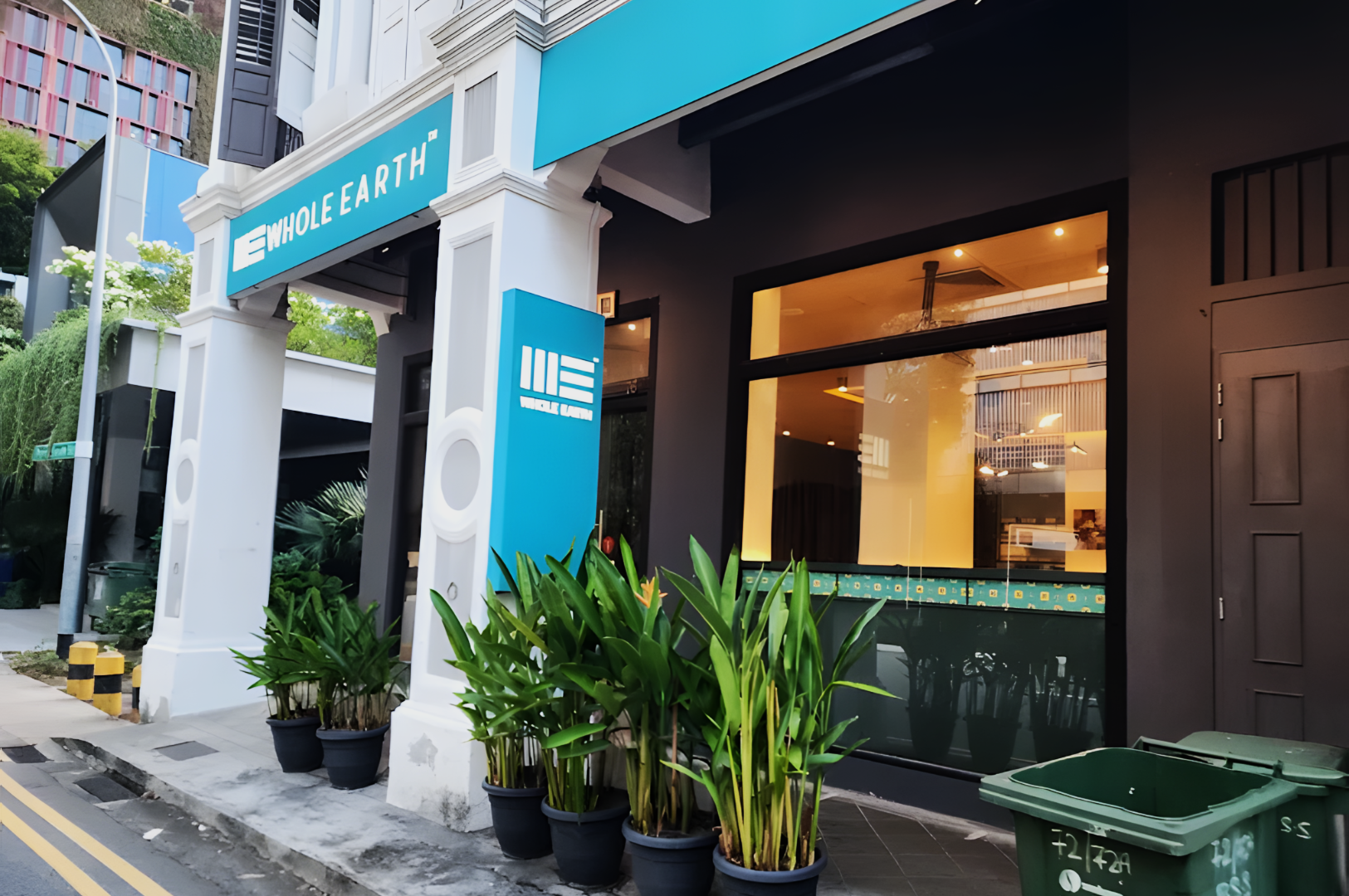 Storefront of a modern restaurant with a bright blue and white sign. Potted plants line the entrance, creating a welcoming and fresh atmosphere.