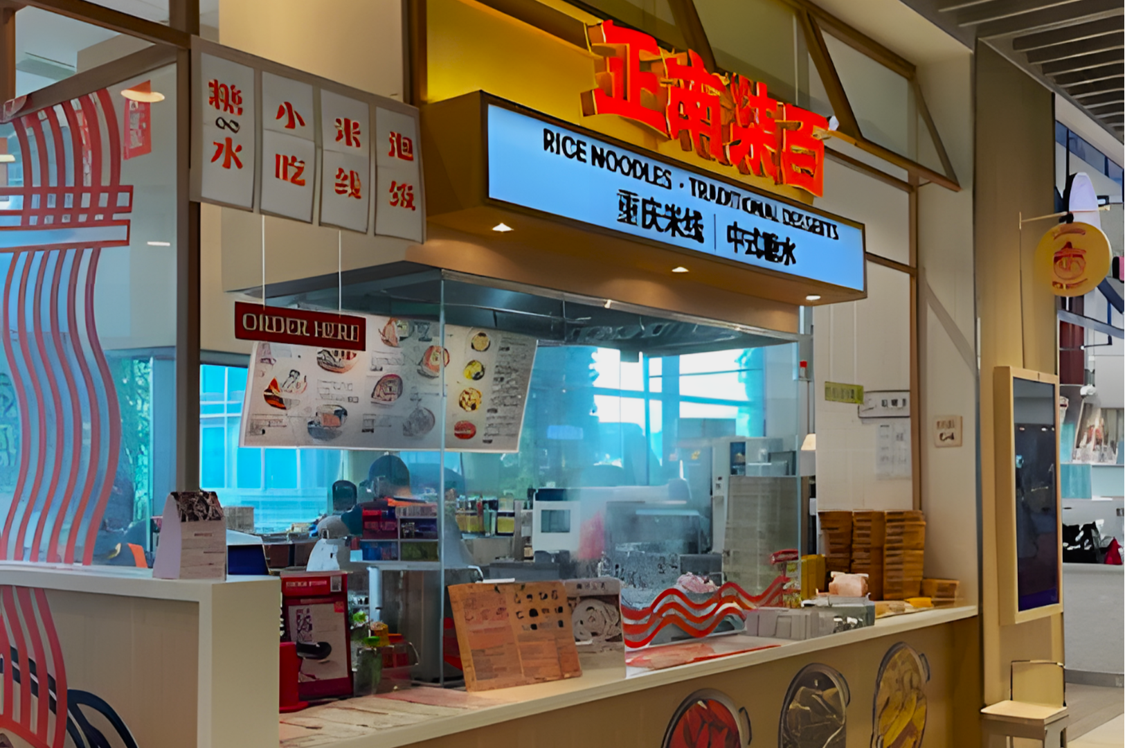 A vibrant food stall in a mall features a bright sign reading "Rice Noodles - Traditional Desserts." Menus and food preparation items are visible inside.