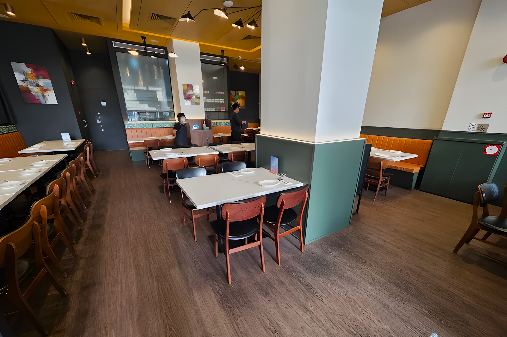 Modern restaurant interior with wooden floors, white tables, and brown chairs. Two servers are setting tables, creating a calm, inviting atmosphere.