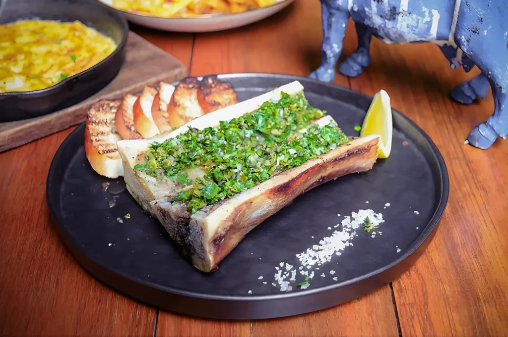 Close-up of gourmet roasted bone marrow topped with fresh herb chimichurri and served with toasted crostini at Bedrock Bar & Grill.